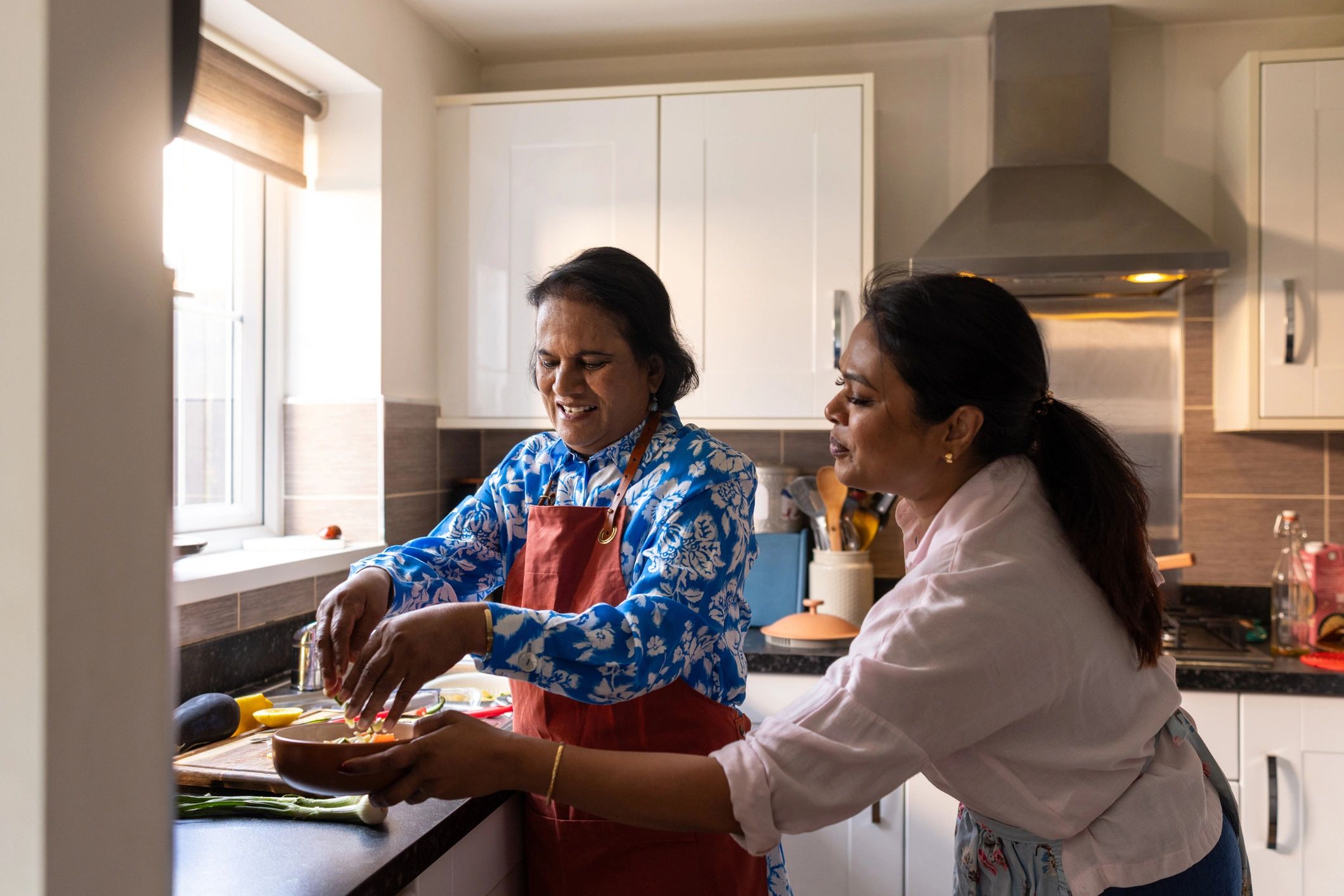 Caregiver and older adult preparing food together in a bright kitchen