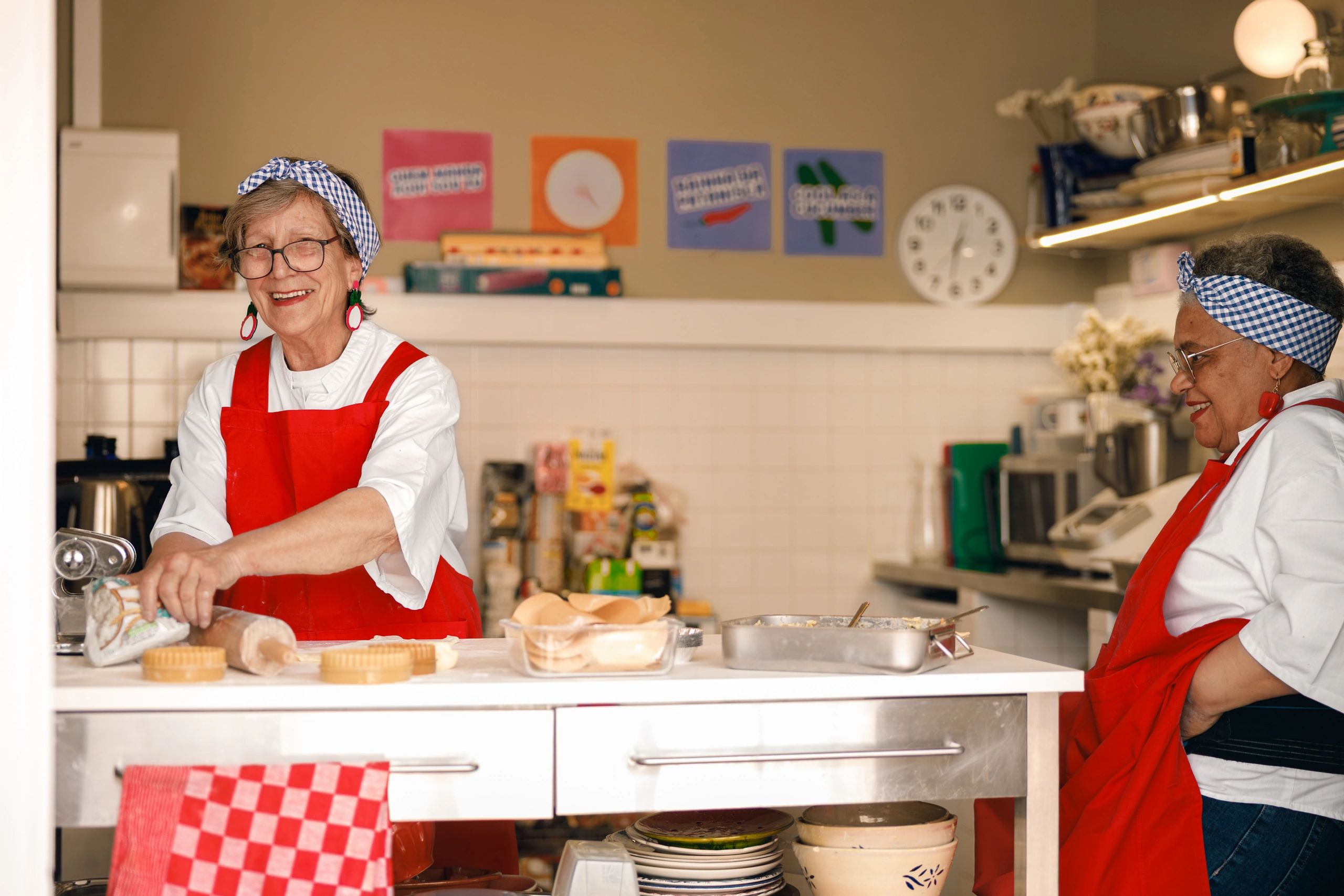 Two senior women smiling and talking while cooking together in a kitchen